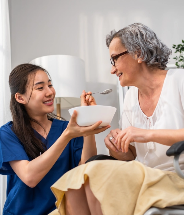 A female caregiver feeding a senior woman sitting on a wheelchair