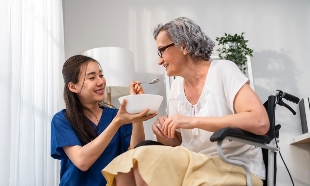 A female caregiver feeding a senior woman sitting on a wheelchair